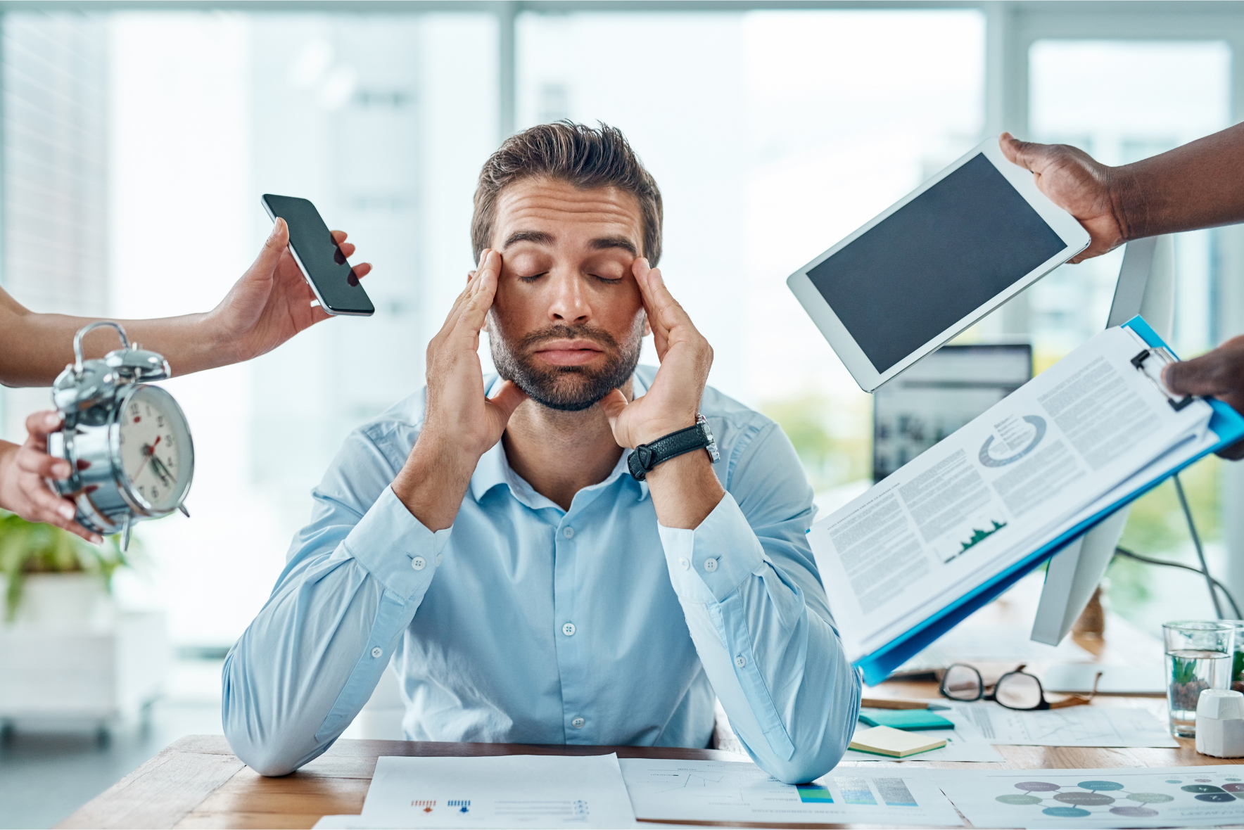 A stressed professional surrounded by various tasks, including a clock, phone, tablet, and paperwork, symbolizing the overwhelming challenges of managing operations without an efficient Flight Scheduler.