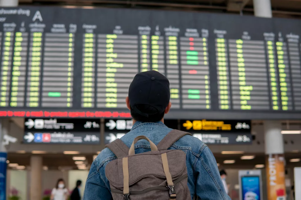 A traveler standing in front of a large airport departures board, examining flight times and destinations. The image reflects the importance of efficient aircraft scheduling to avoid delays and ensure smooth operations.